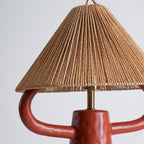 Close view of the terracotta ceramic arms and the lower edge of the woven shade on this Clérachic lamp, with a brass stem between.