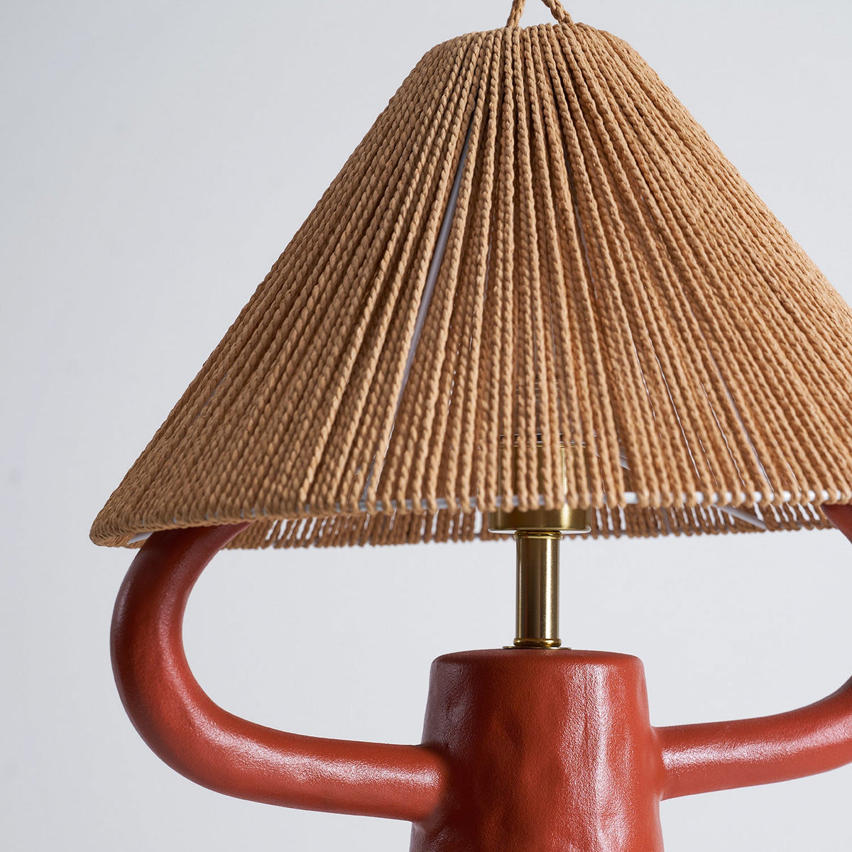 Close view of the terracotta ceramic arms and the lower edge of the woven shade on this Clérachic lamp, with a brass stem between.
