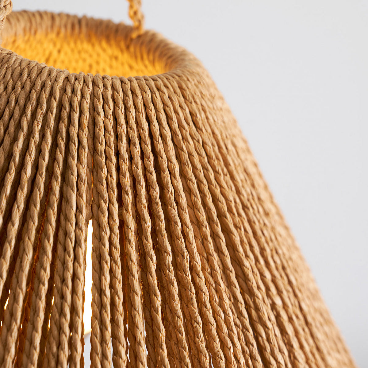 Close view of the shade's open top, warm glow inside and braided loop above, on this Clérachic table lamp.