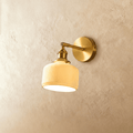 Clérachic brass wall lamp with a ribbed ceramic shade glowing a warm yellow, mounted on a plaster wall.