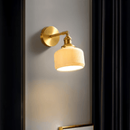 Clérachic brass wall lamp with a ribbed ceramic shade casting warm light on a grey wall between dark curtains.