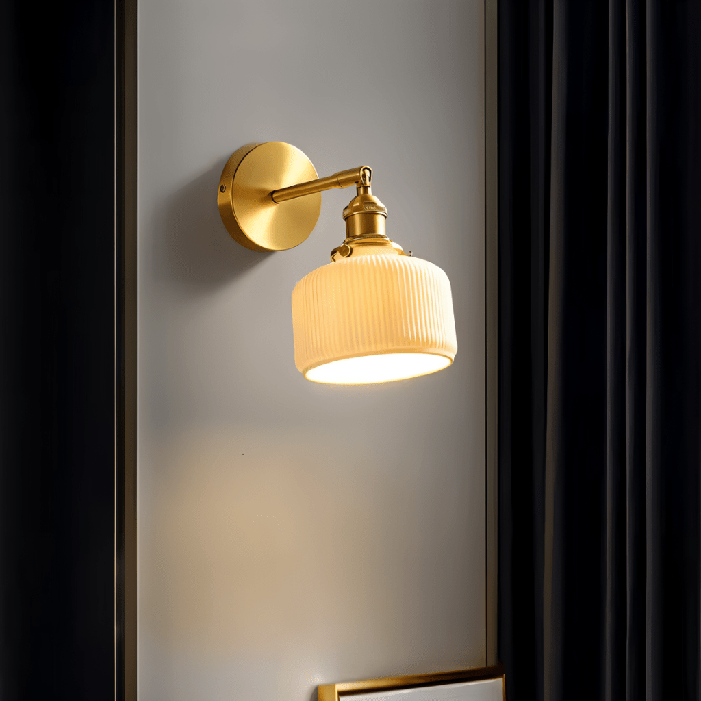 Clérachic brass wall lamp with a ribbed ceramic shade casting warm light on a grey wall between dark curtains.