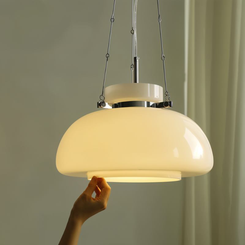 Hand touching the lit rim of a Clérachic white glass dome pendant, with chrome chain links and a white top cap.