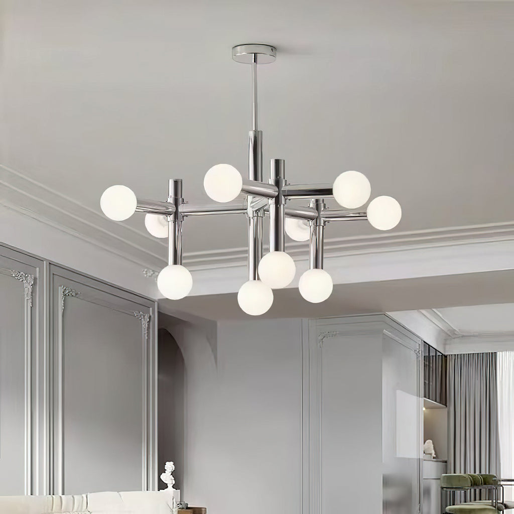 Low view up at a Clérachic chrome chandelier with frosted spheres, hanging in a panelled grey room with a moulded ceiling.