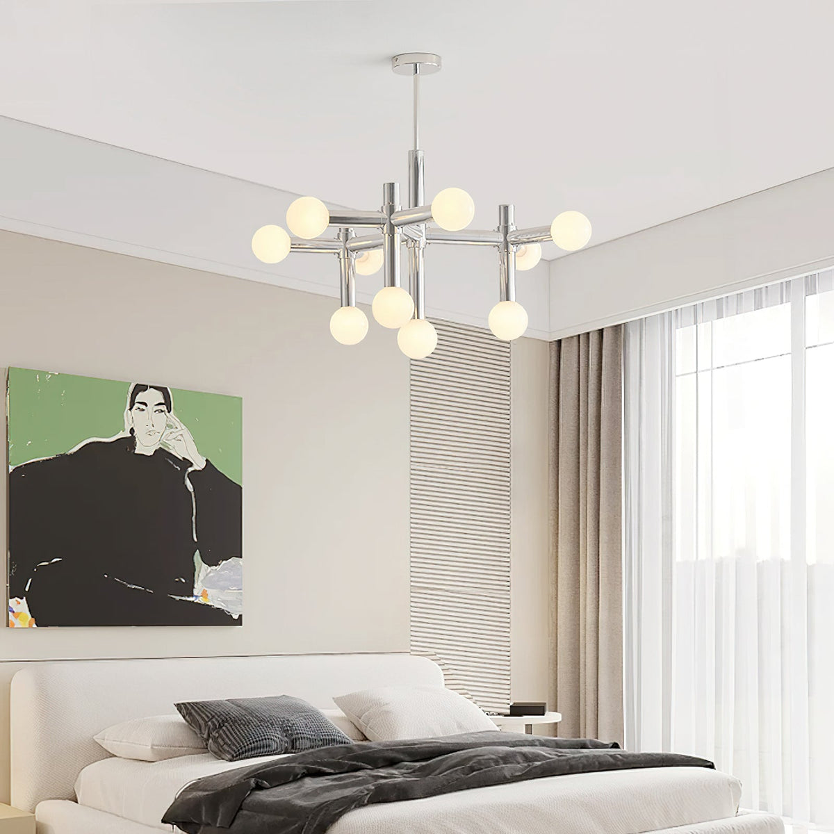 A Clérachic chandelier glowing high in a bedroom with a low white bed, grey bedding and a green portrait print on the wall.