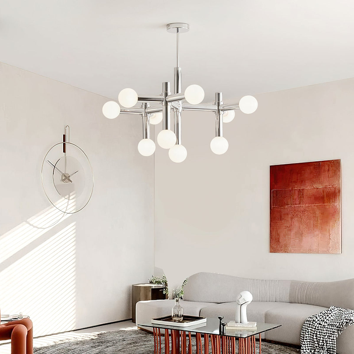 Lit Clérachic chandelier with chrome arms hanging in a pale living room, near a rust-red painting and a round wall clock.