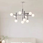 A Clérachic chandelier hanging above a bed with a fluted cream headboard, its chrome arms and white globes lit softly.