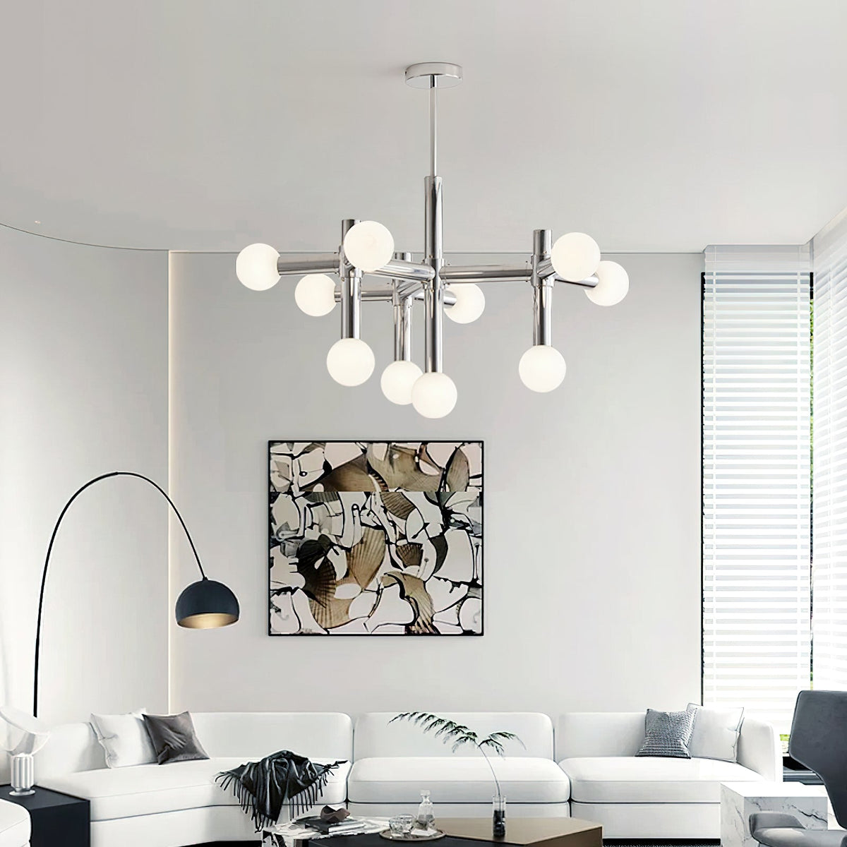 The Clérachic chandelier lit above a white sofa, with an arched black floor lamp and an abstract print on the wall.