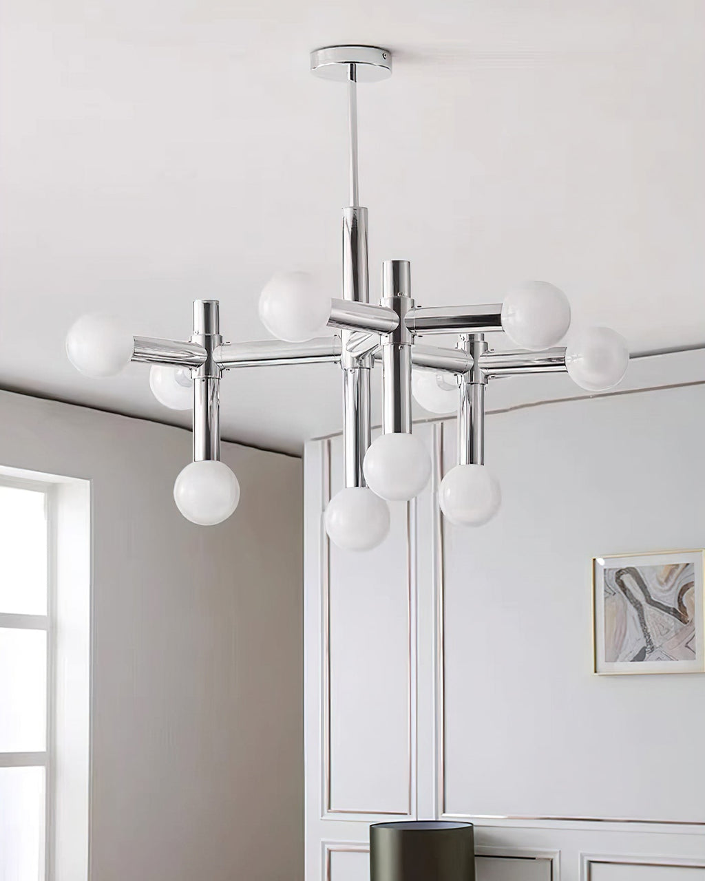 Portrait view of the Clérachic chandelier, its ten spheres glowing against a white panelled wall with a small framed print.
