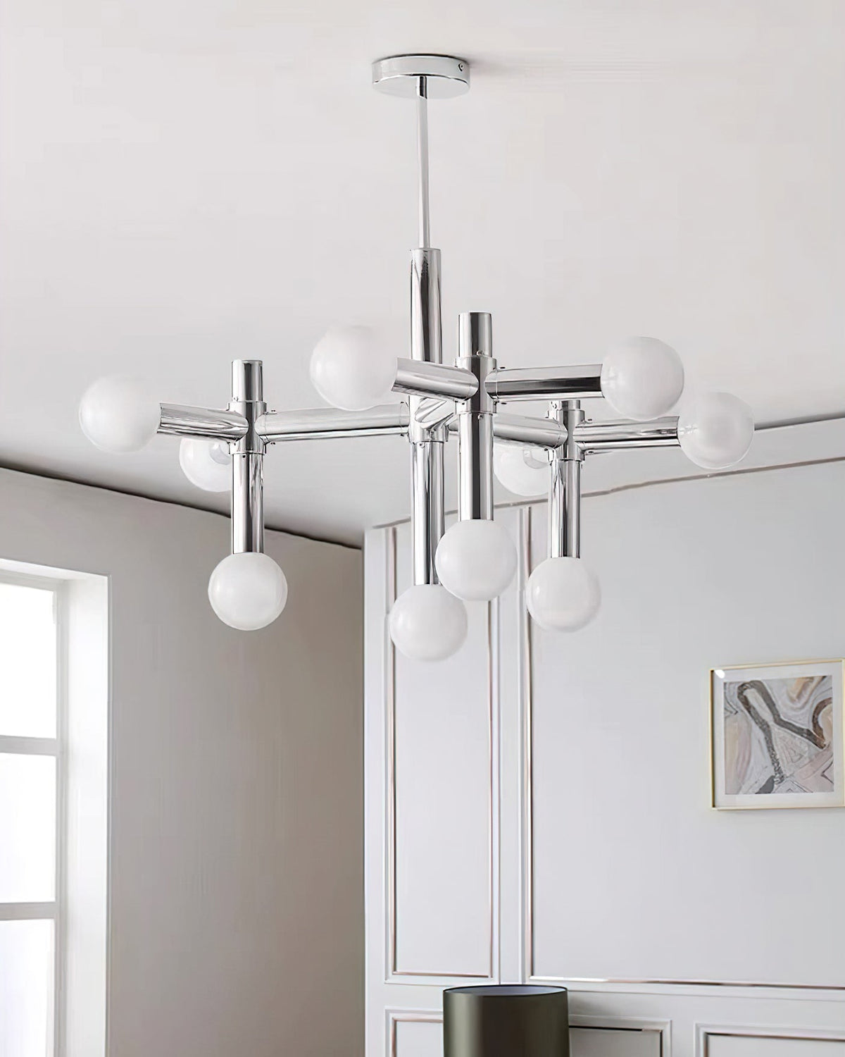Portrait view of the Clérachic chandelier, its ten spheres glowing against a white panelled wall with a small framed print.