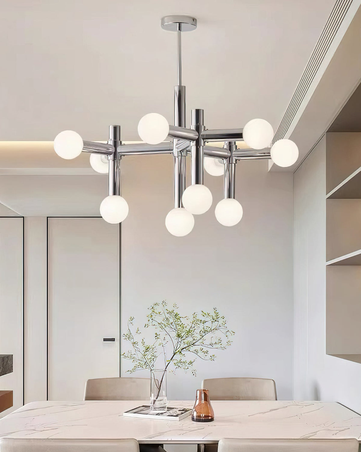 Clérachic chandelier hanging over a marble dining table set with a vase of green stems, seen from below.