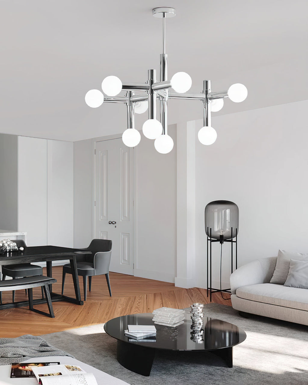 A Clérachic chandelier above a dark dining table and a round black coffee table, in a room with herringbone wood flooring.