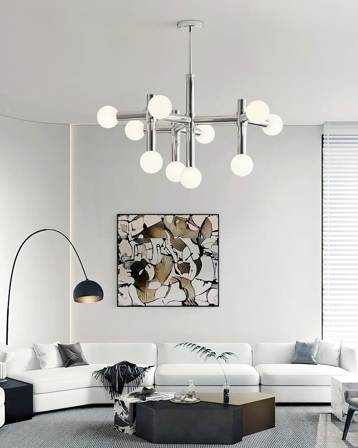 Portrait view of a lit Clérachic chandelier over a white curved sofa, with an arc floor lamp and a framed abstract artwork.