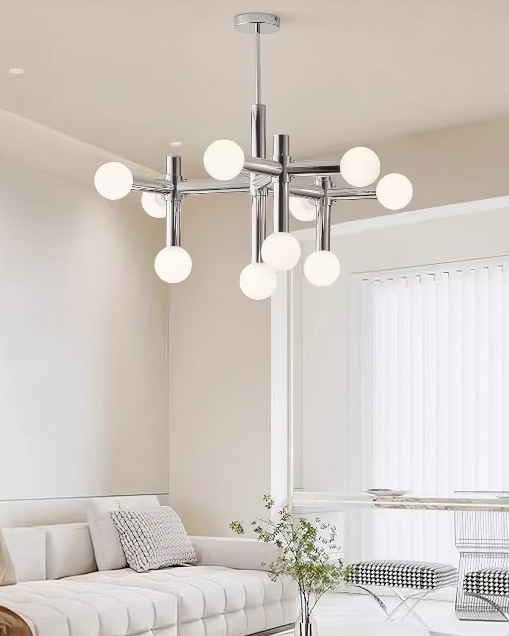The Clérachic chandelier in a bright living room, hanging above a tufted cream sofa beside a window with vertical blinds.