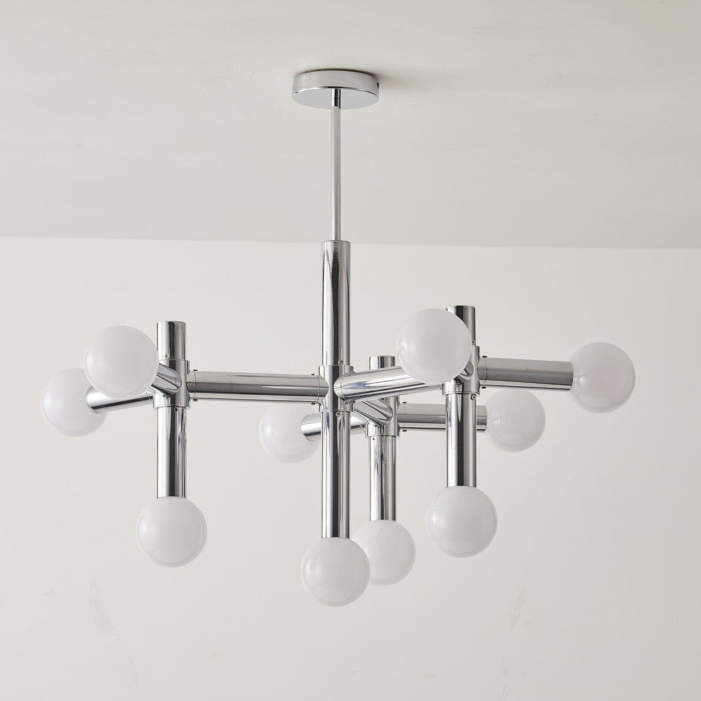 Unlit Clérachic chandelier against a pale wall, its chrome crossing arms and ten white globes hanging from a thin rod.
