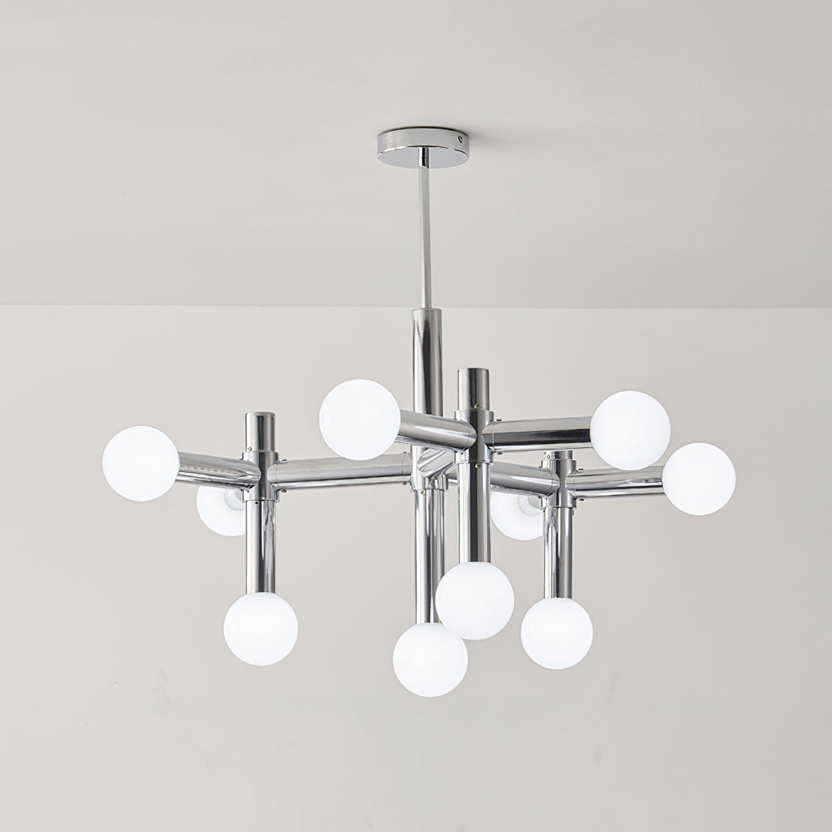 The same Clérachic chandelier switched off, with its ten frosted white globes and chrome crossing arms on a pale grey wall.
