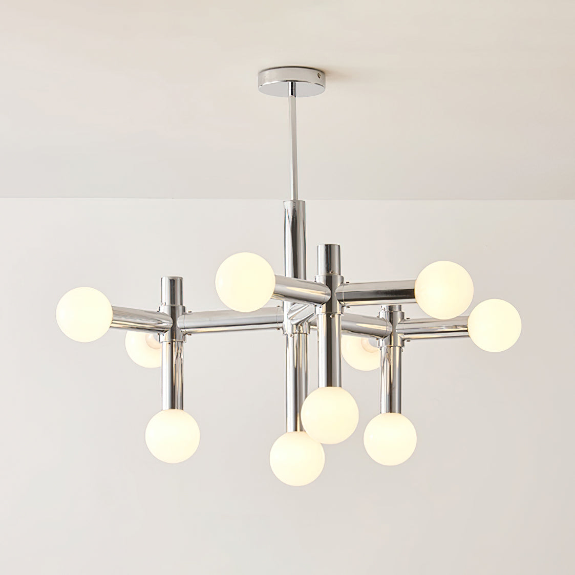 Clérachic chandelier lit warm, the spheres giving off a gentle glow along the polished chrome arms and central stem.