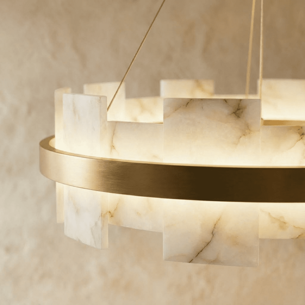 Close view of a Clérachic chandelier showing veined alabaster panels glowing beside a brushed brass ring.