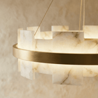 Close view of a Clérachic chandelier showing veined alabaster panels glowing beside a brushed brass ring.