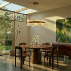 Clérachic circular alabaster and brass chandelier hung over a round walnut dining table in a sunlit room.