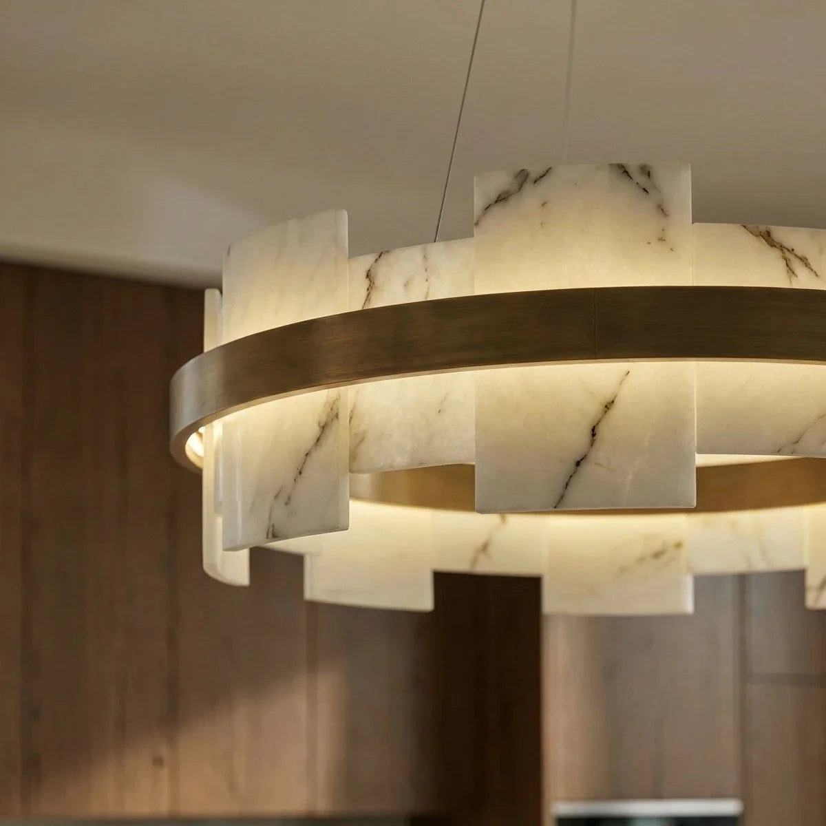 Underside view of a Clérachic chandelier, its alabaster segments glowing around a brushed brass ring in a kitchen.