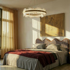 Clérachic circular alabaster chandelier lit above a bed with a scalloped headboard and sheer golden curtains.