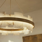 Low-angle view of a Clérachic alabaster and brass ring chandelier glowing softly beside a framed artwork.