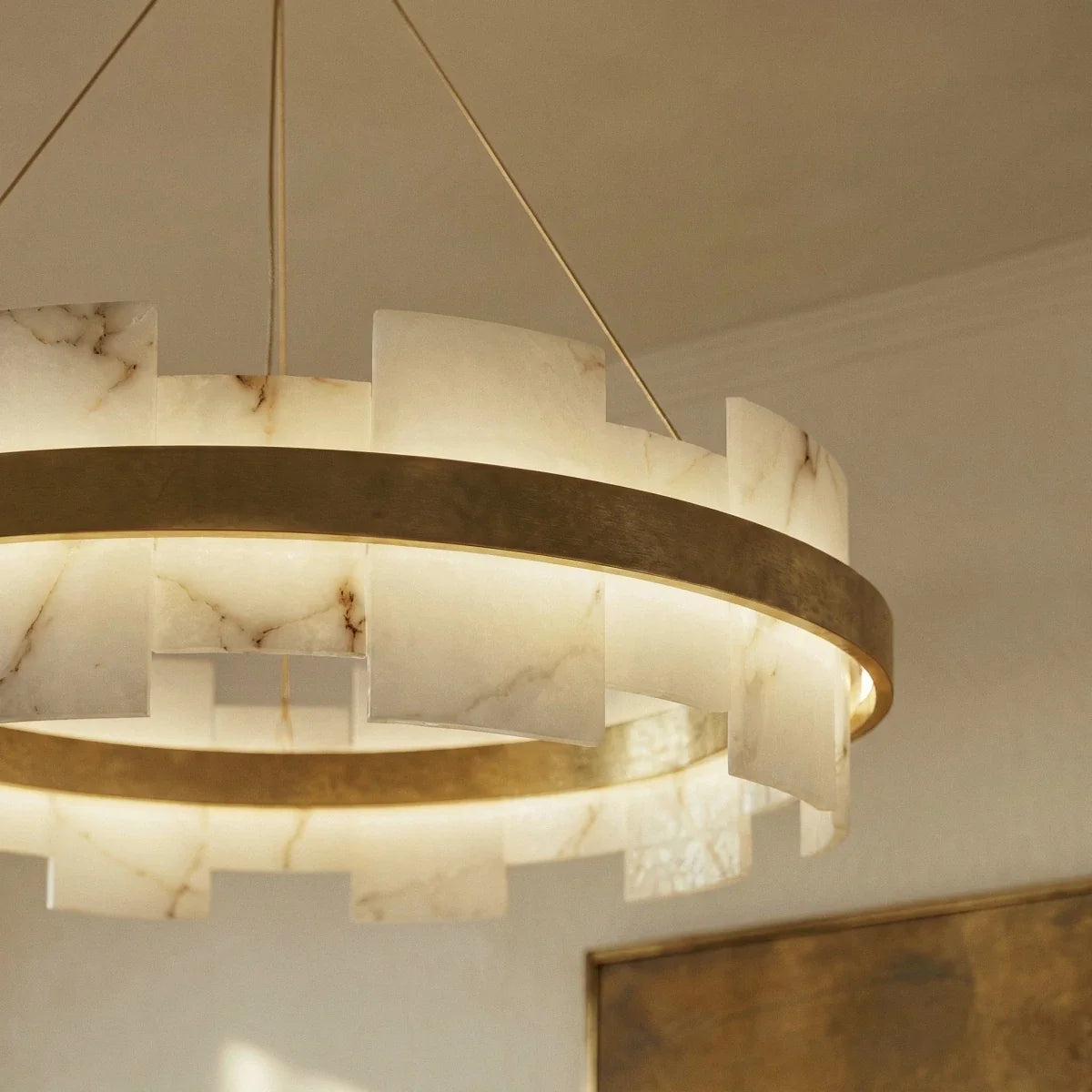Low-angle view of a Clérachic alabaster and brass ring chandelier glowing softly beside a framed artwork.