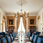 Large dining hall with blue chairs along a laid table, and a Clérachic antique brass chandelier under a carved ceiling rose.