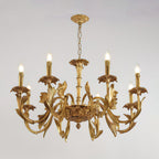 Clérachic brass chandelier lit, hanging from a chain and ornate canopy against a pale grey backdrop.