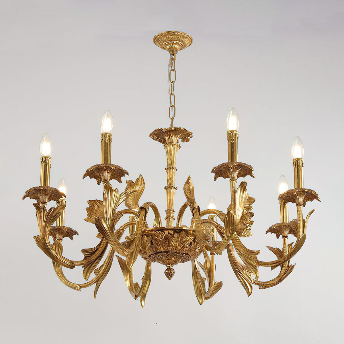 Clérachic brass chandelier lit, hanging from a chain and ornate canopy against a pale grey backdrop.