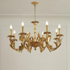 Clérachic brass chandelier hanging in a room with a white panelled wall and cornice, its candle bulbs lit.