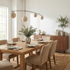 A nickel-finish Clérachic chandelier arcs above a wood dining table set with eucalyptus and stoneware plates.