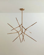 Clérachic branching rod chandelier in brushed gold, angular arms radiating from a slim stem and round ceiling canopy.