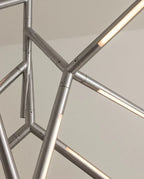 Clérachic close detail of chrome chandelier arms joined at angles, each rod carrying a glowing strip of warm light.