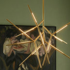 Clérachic close view of a gold branching rod chandelier, its lit rod arms crossing in front of a framed figure painting.
