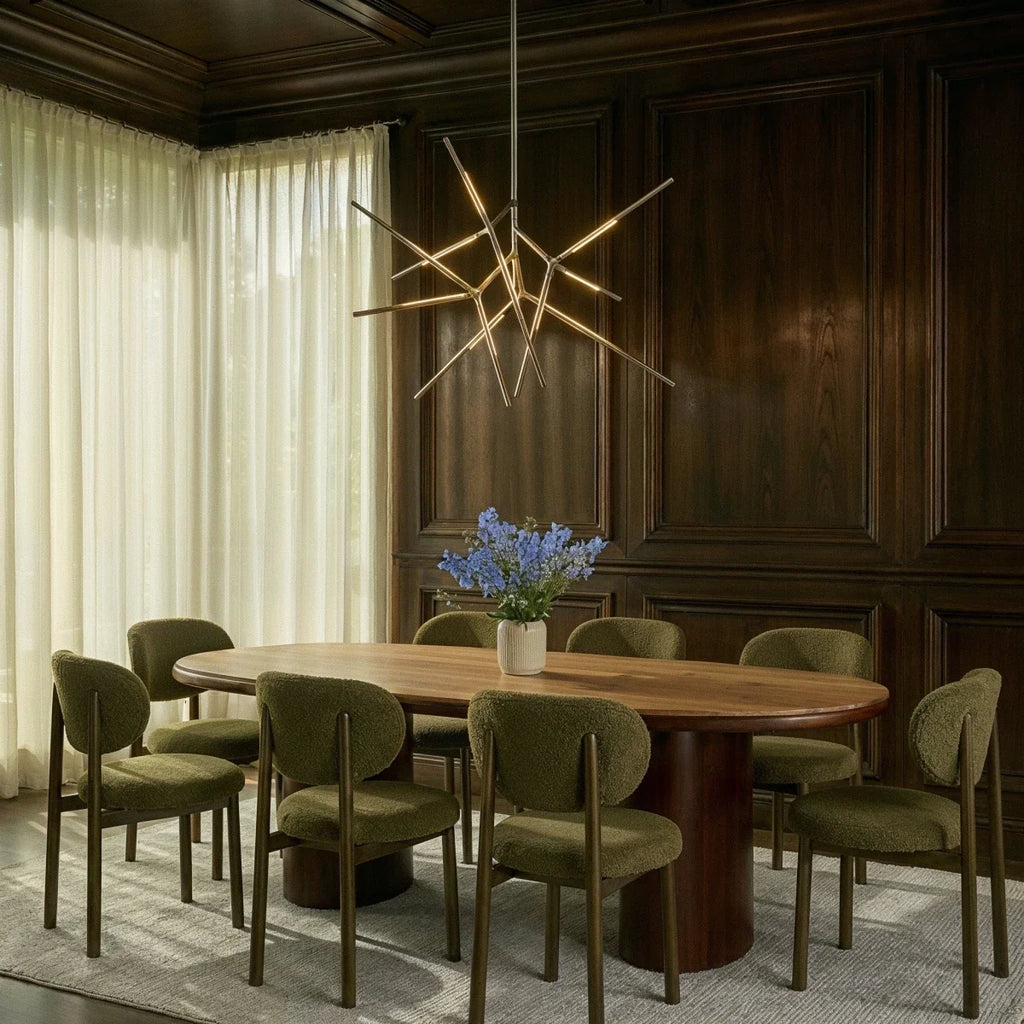 Clérachic satin metal rod chandelier lit above an oval wooden dining table, in a room of dark wood panelling and olive chairs.