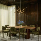 Clérachic satin metal rod chandelier lit above an oval wooden dining table, in a room of dark wood panelling and olive chairs.