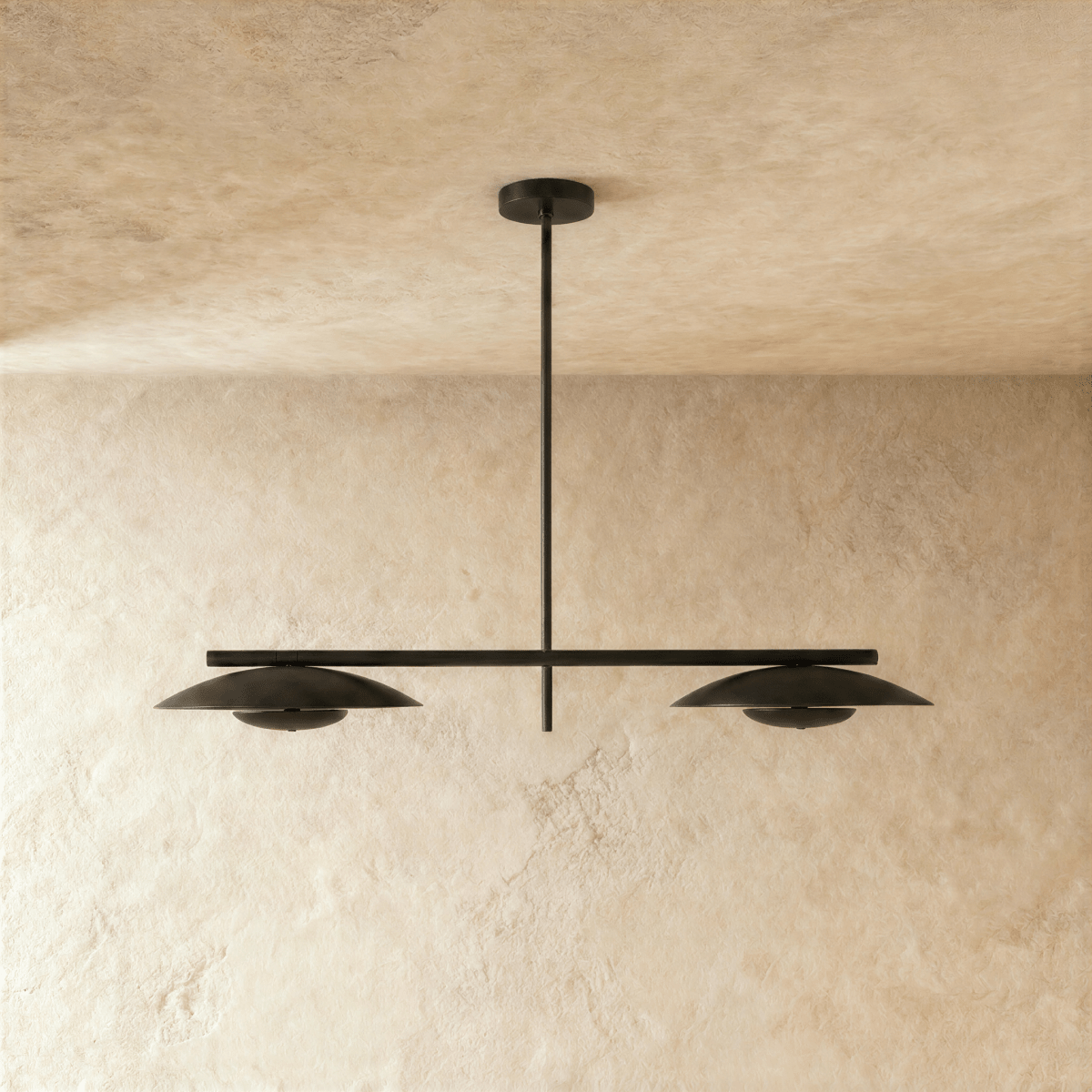 Clérachic chandelier in matte black, front view of the paired disc shades against a plaster wall.