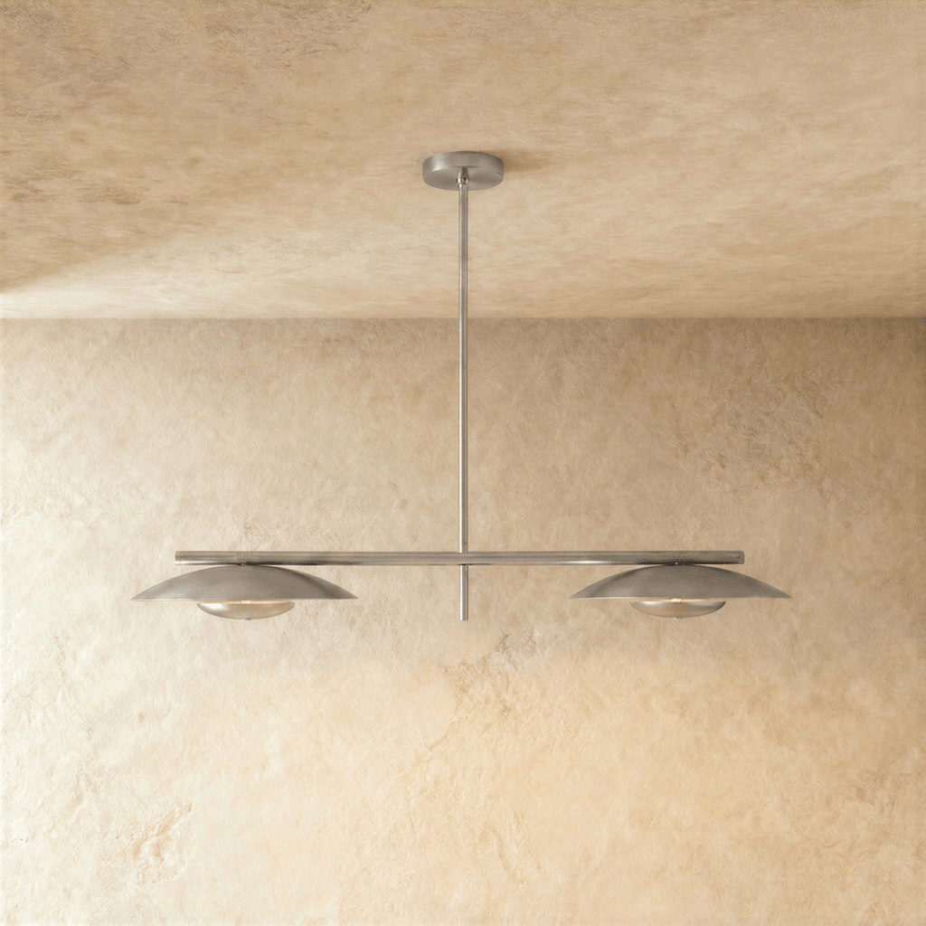 Clérachic chandelier in chrome, twin disc shades hung from a slender bar against a plaster wall.