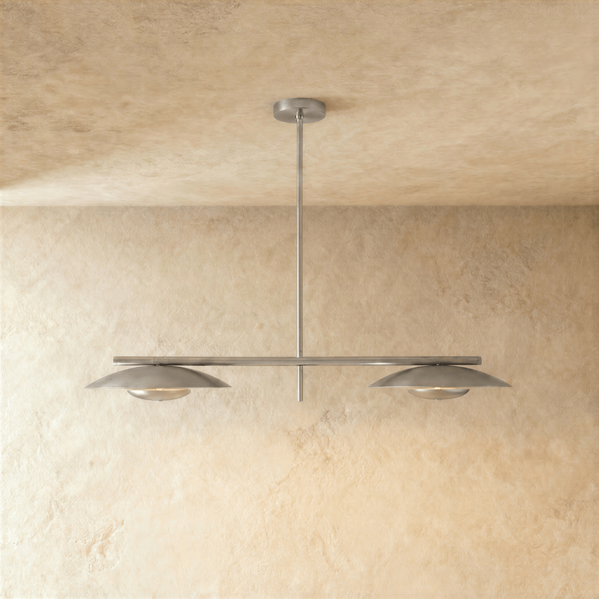 Clérachic chandelier in chrome, twin disc shades hung from a slender bar against a plaster wall.