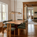 Clérachic chandelier in brass over a walnut dining table beside a doorway framed in stained wood.