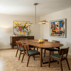 Clérachic chandelier in brass over a round dining table set beneath two colorful abstract paintings.