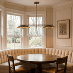 Clérachic chandelier in brass lighting a curved banquette table in a bay-window breakfast nook.