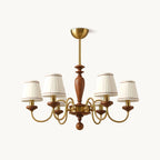 Gold and walnut chandelier with pleated white fabric shades on curved brass arms, hung from a gold canopy on a plain white backdrop, from Clérachic.