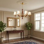 Clérachic chandelier hung from a ceiling rose in a panelled hallway, with a gilt mirror, a console table and two potted plants.