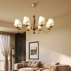 Clérachic chandelier in a warm-toned living room, its white pleated shades glowing above a sofa, a sheer curtain and a framed photo.