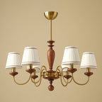 Gold and walnut Clérachic chandelier on a warm beige backdrop, six pleated shades on curved brass arms around a turned wooden stem.