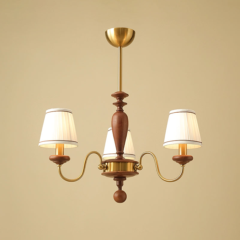 Three-light gold and walnut Clérachic chandelier, its S-shaped brass arms carrying lit pleated shades on a warm beige background.