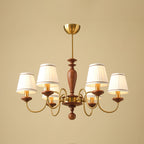 Six-light Clérachic chandelier in gold and walnut, hung from a short brass canopy with the shades lit against a sand-coloured backdrop.